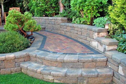 Curved stone patio with steps, retaining walls, and lush garden plants in Ogden, UT